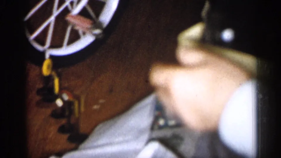 A person's hand works with small toy bicycle parts near a white-spoked wheel in 1959 Michigan home-movie footage.