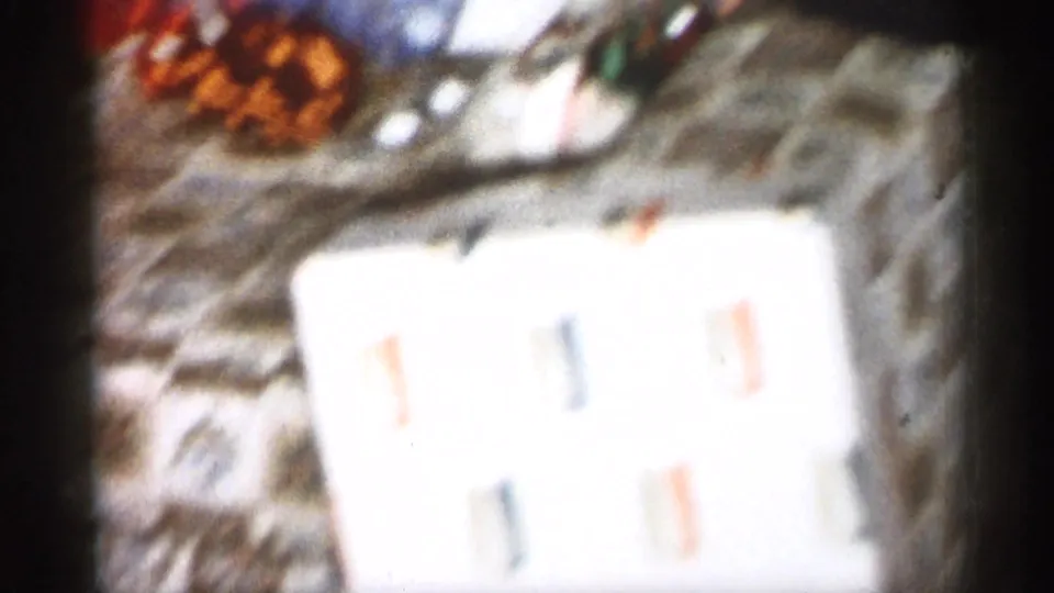 Soft 1959 Michigan 8mm frame showing wrapped Christmas gifts and paper on a wooden floor inside a private home.