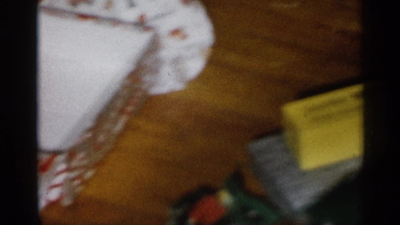 1959 Michigan home-movie frame with a yellow box, patterned holiday material, and floor-level household clutter.
