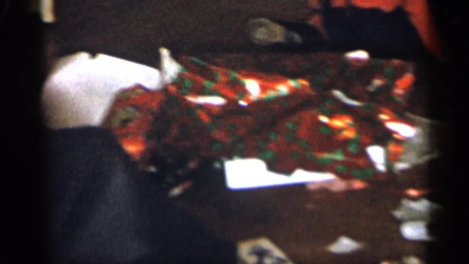 1959 Michigan 8mm frame showing a person partly visible beside shiny Christmas wrapping and a white package in a private home.