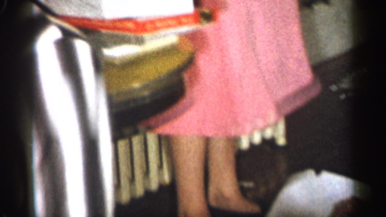 Partial view of guests in a room, including a woman in a pink dress standing near a radiator.