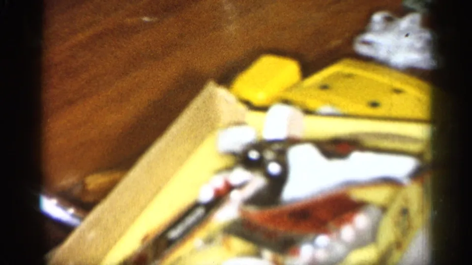 1959 Michigan home-movie frame showing a wooden table with a yellow object, small accessories, and scattered party items.