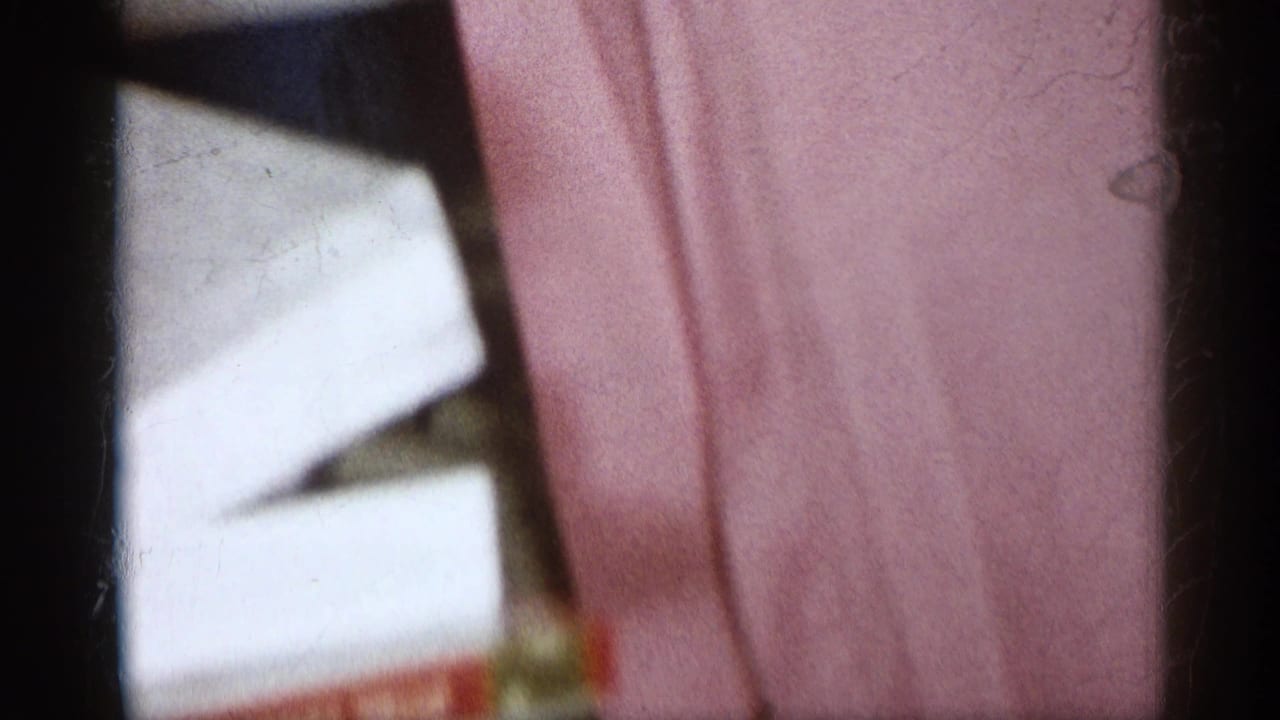1959 Michigan home-movie frame showing a close, cropped view of a pink dress near holiday wrapping inside a private home.