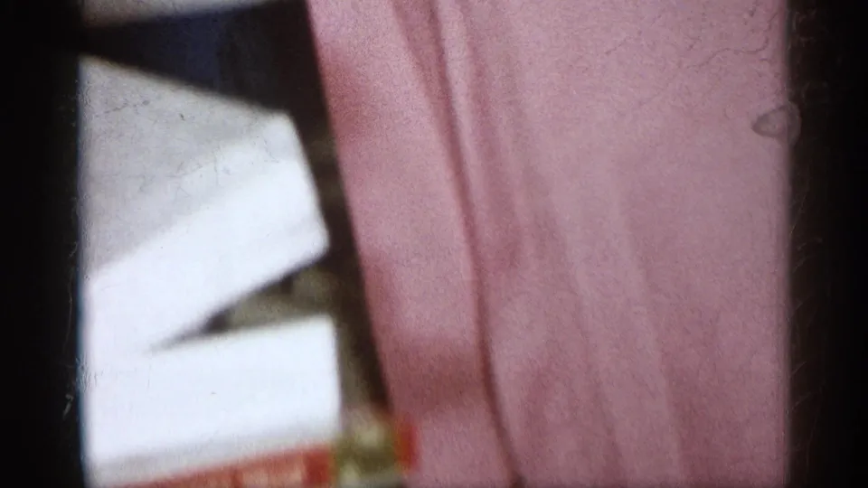 1959 Michigan home-movie frame showing a close, cropped view of a pink dress near holiday wrapping inside a private home.