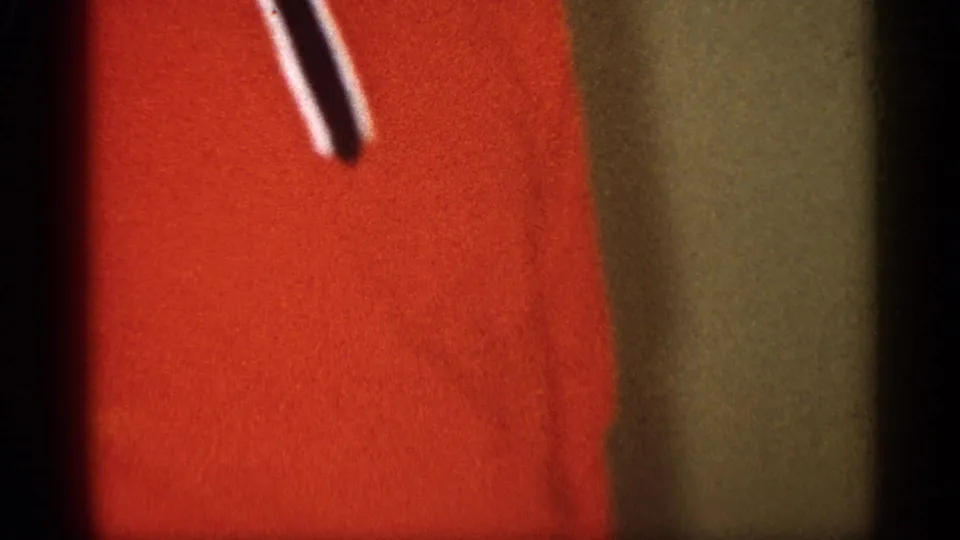 Close-up of red fabric or clothing within the soft handheld 8mm frame, with little surrounding context visible.
