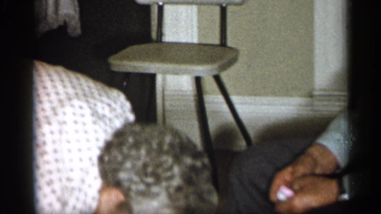 Person in a striped shirt leans near a small stool inside a private room.