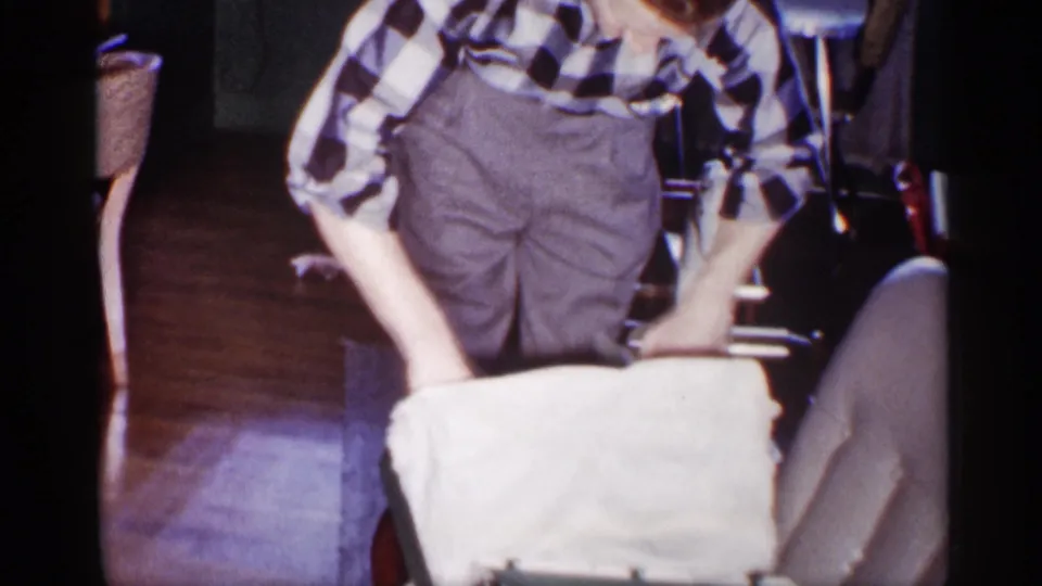 The man continues leaning over the opened box or wrapping in the dim Michigan home interior.