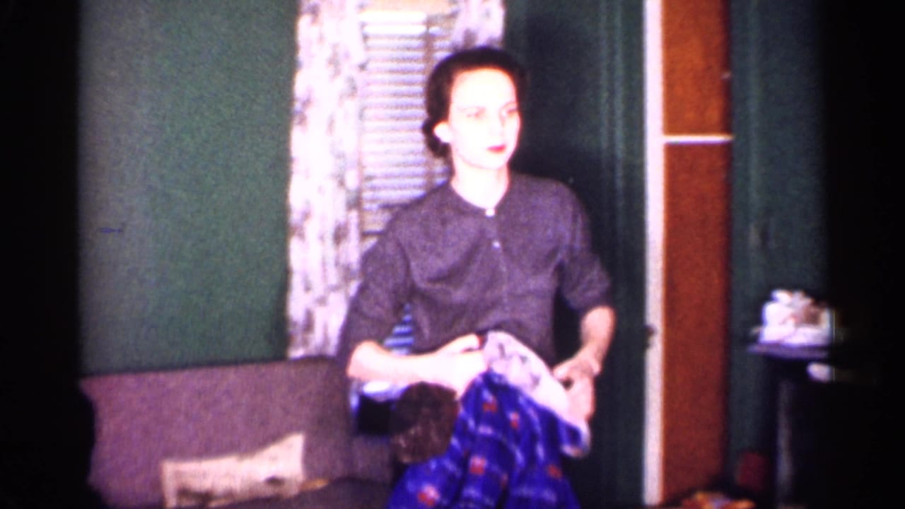 1959 Michigan interior frame with a woman holding folded clothing in a living room or sitting room.