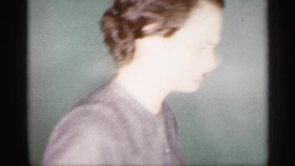 Close, overexposed 1959 Michigan home-movie frame of a woman in profile inside a private room.