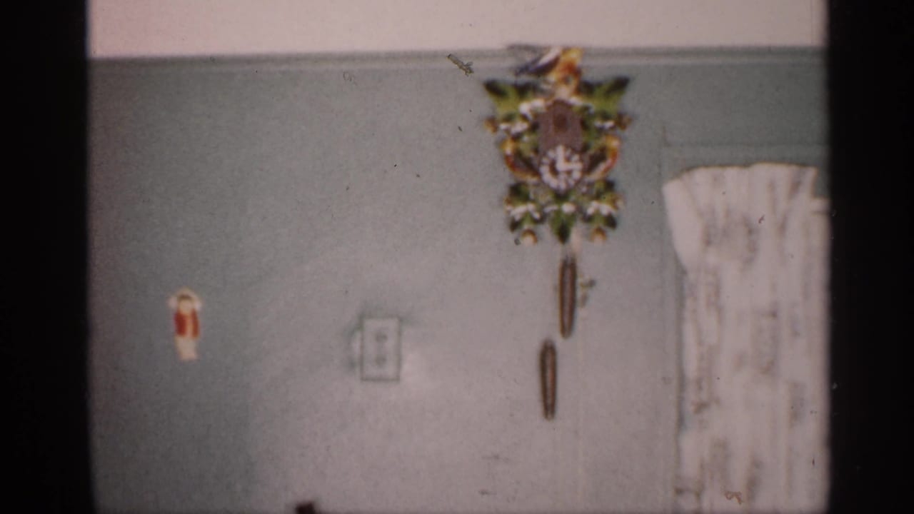 A close home-movie view of a decorative cuckoo clock and curtain inside a Michigan residence, with soft 8mm focus and visible gate edge.