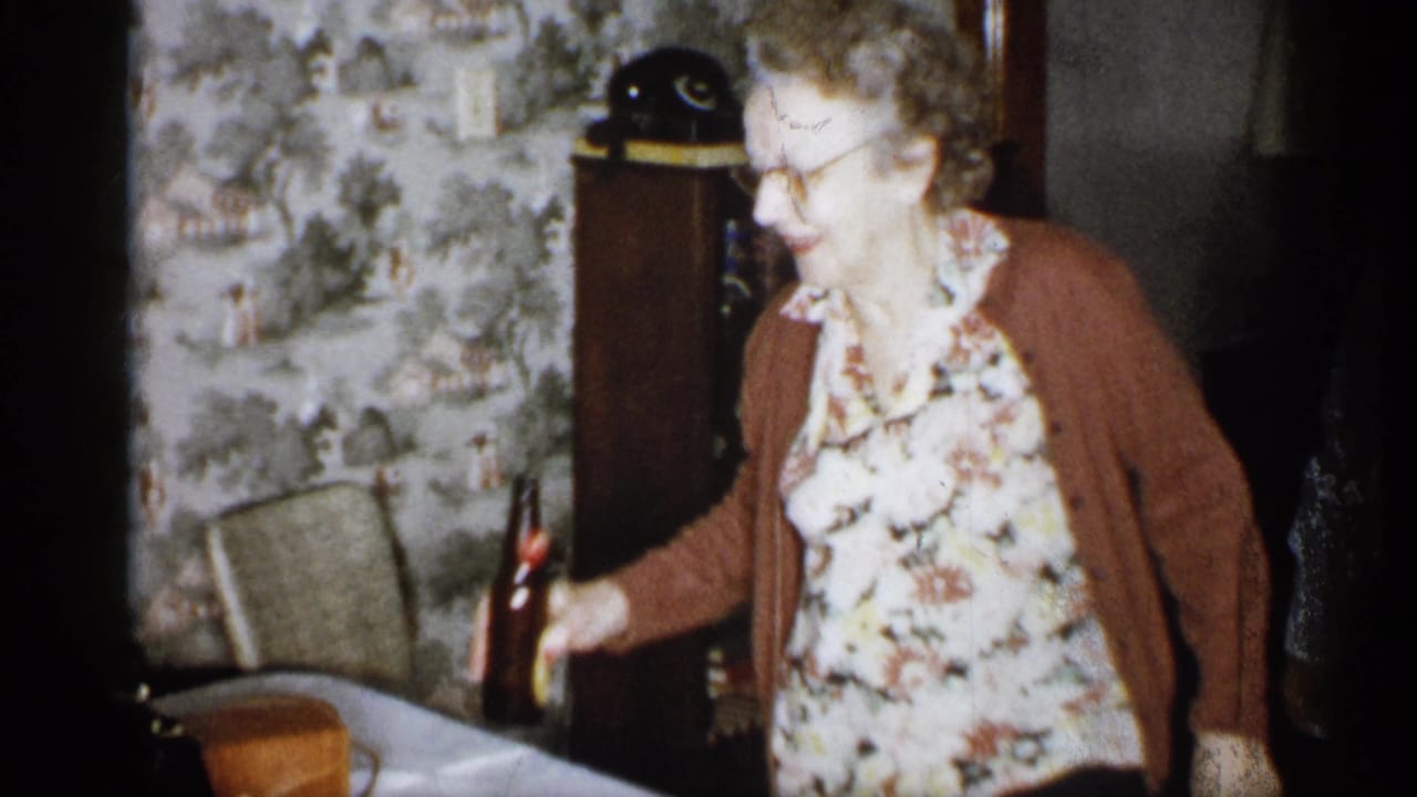 Older woman reaches toward a dark bottle on a table near a chair and cabinet.