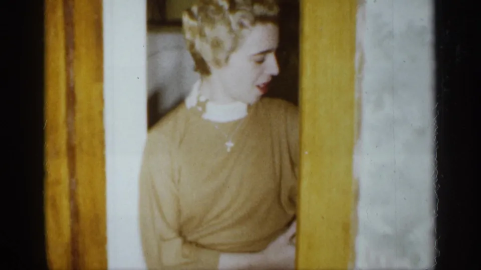 A young woman in a yellow top or sweater appears by a wood-trimmed doorway in this 1959 Michigan home-movie frame.