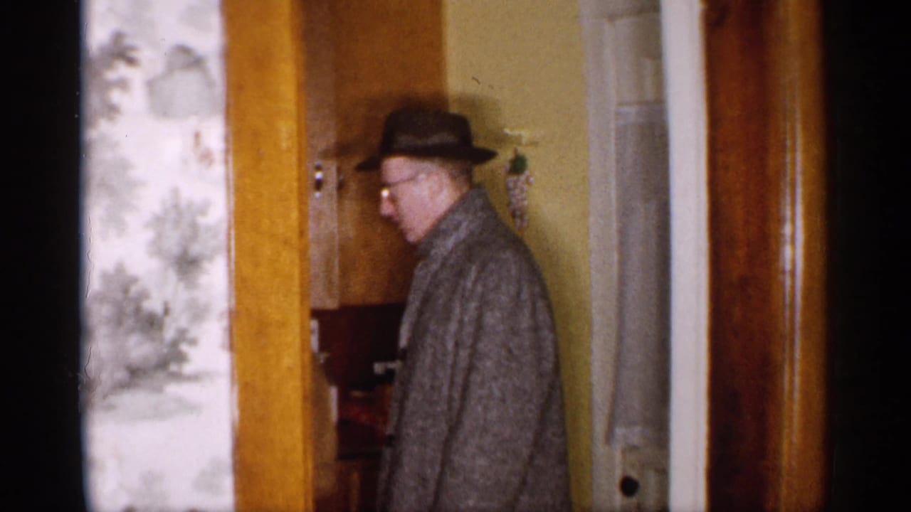 A man in a fedora and gray coat turns near a doorway inside a 1959 Michigan private home.
