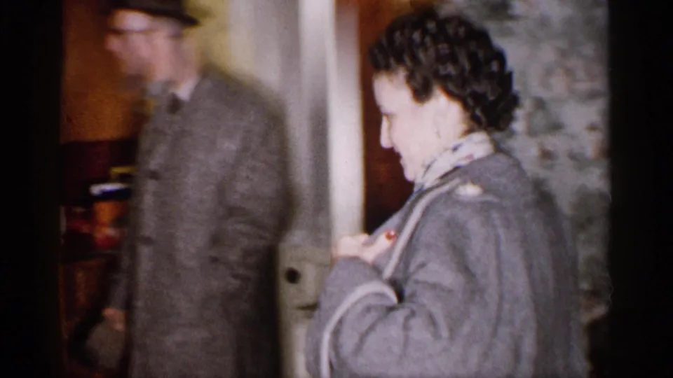 A woman in a gray coat and scarf enters a Michigan home as a man in a hat and overcoat follows in the doorway.