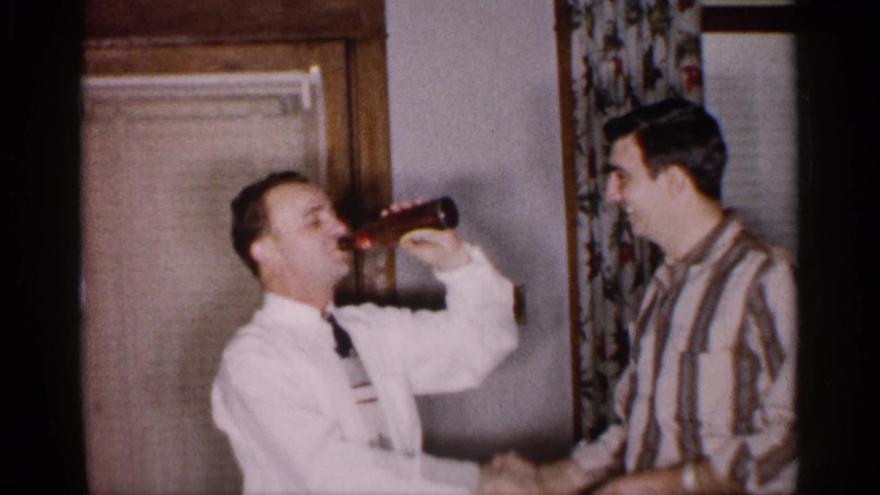 Two adult men indoors shake hands while one drinks from a brown bottle.