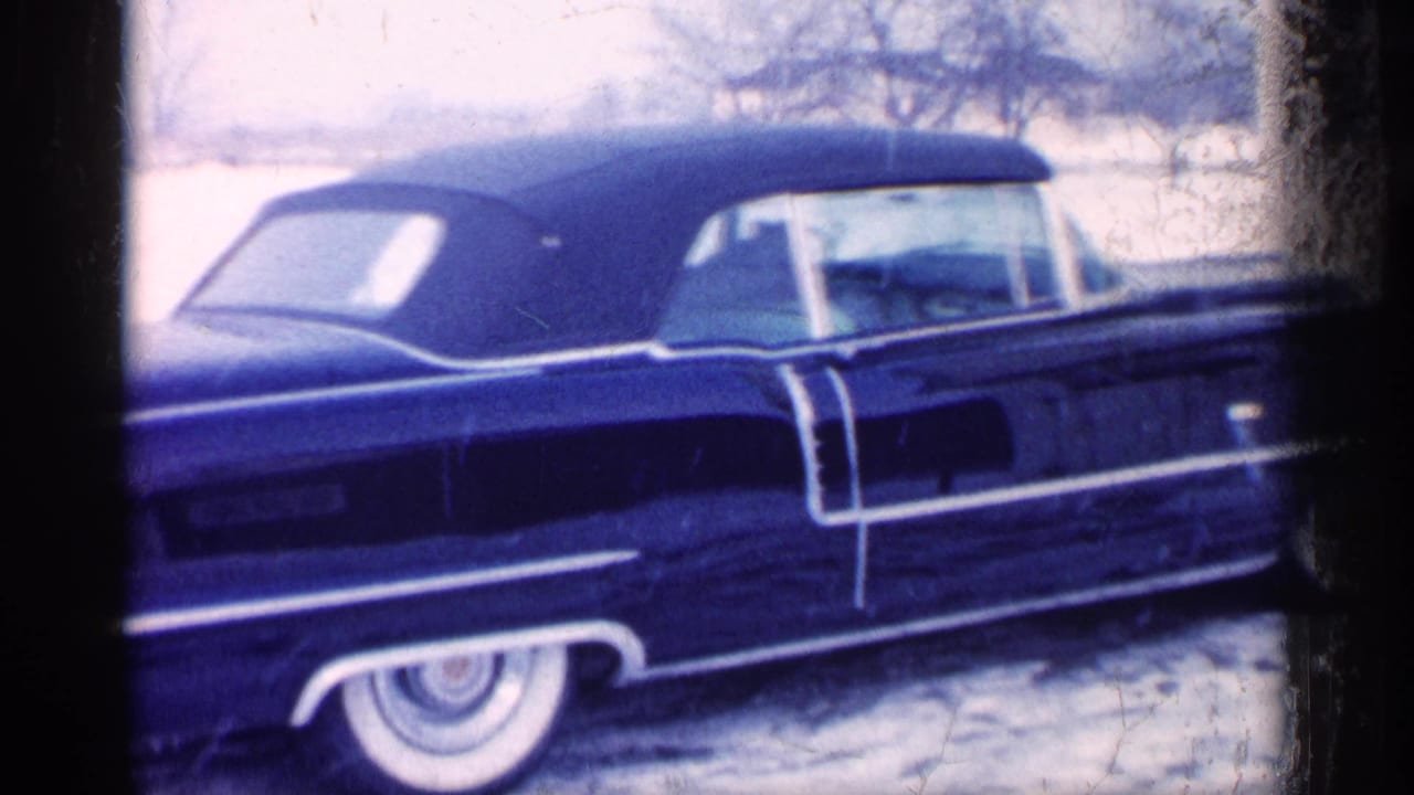 Side view of the same dark convertible in snow, framed by dark film edges.