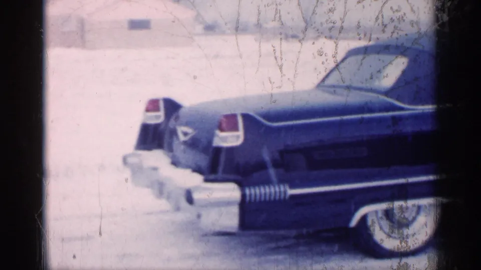 Michigan 1959 home-movie frame showing the rear quarter of a dark blue convertible in a snowy yard or roadside setting.
