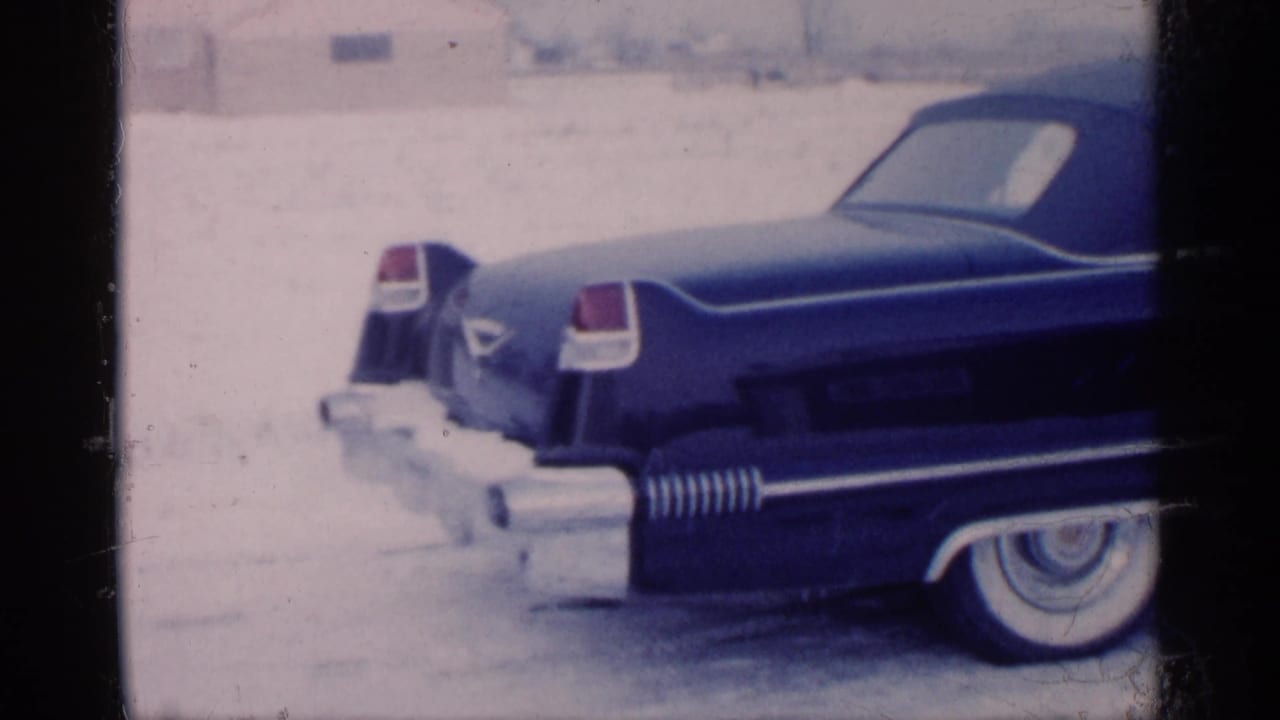 Dark blue tailfinned convertible parked on snowy ground, seen from the rear side.