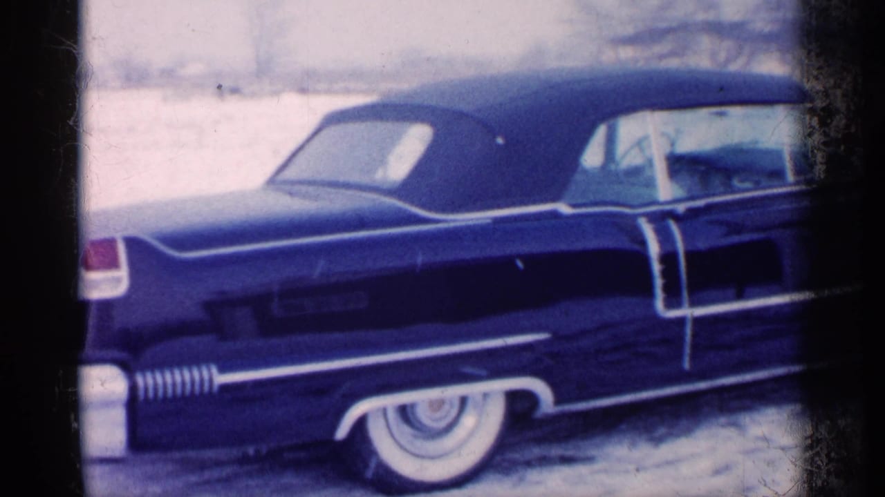 1959 Michigan frame of a dark blue 1950s-style convertible in snow, with prominent chrome trim and whitewall tire visible.
