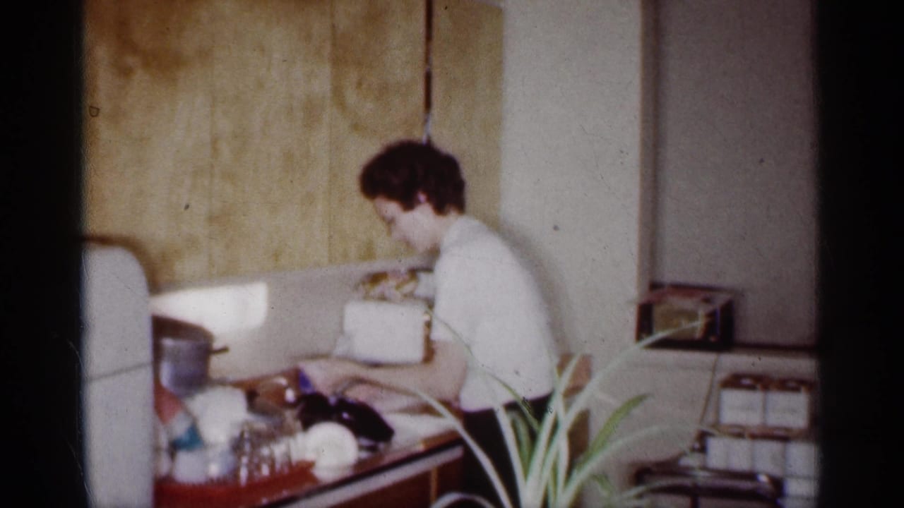 Woman washing dishes at a kitchen sink beside a white refrigerator.