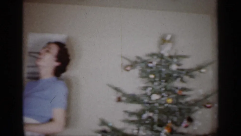 1959 Michigan home-movie frame showing a woman beside a decorated Christmas tree in a private living room.