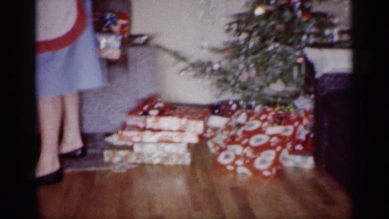 1959 Michigan home-movie frame showing wrapped Christmas presents beneath a decorated tree in a private home.