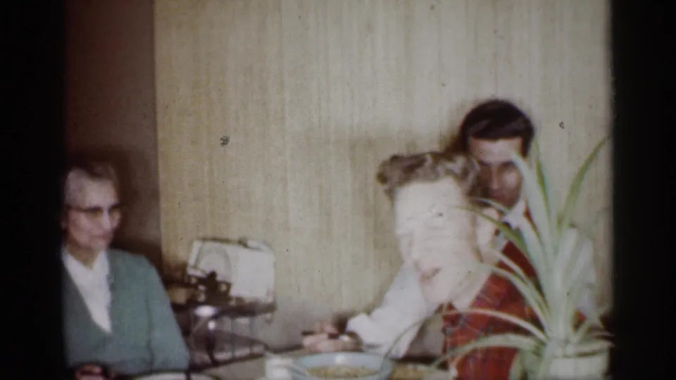 1959 Michigan home-movie frame showing family members seated at a dining table in a private interior.