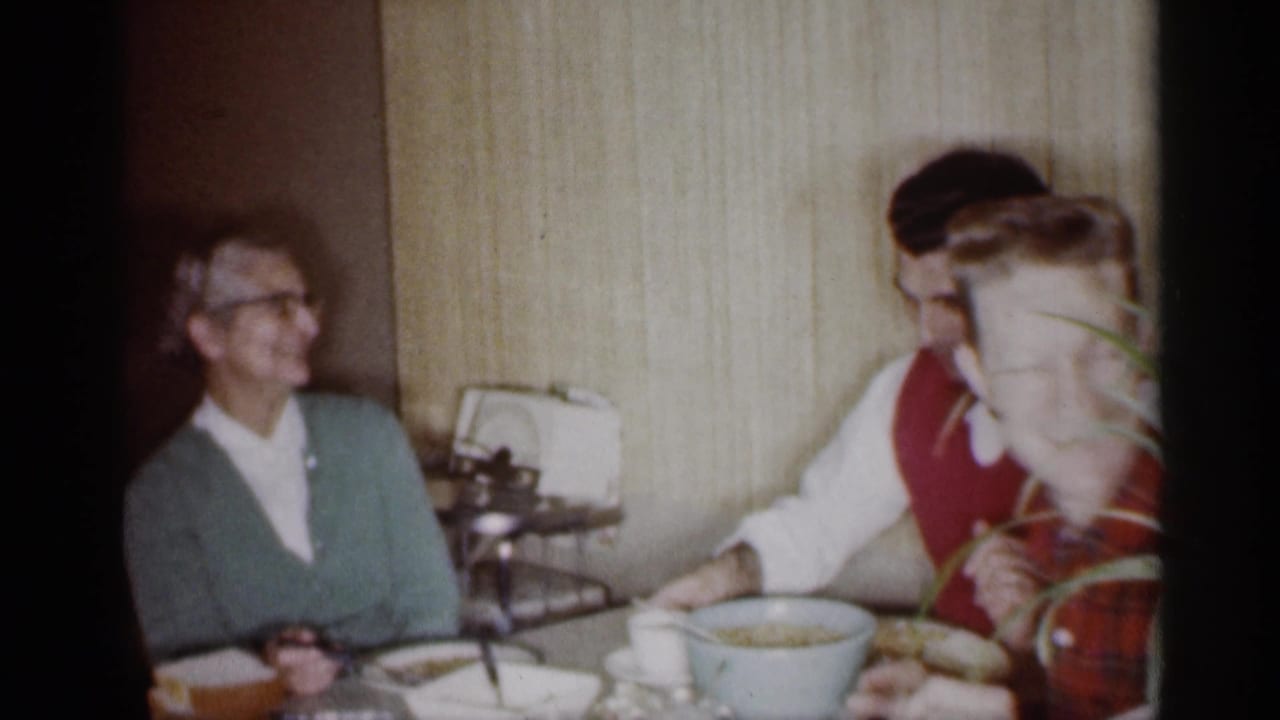 Older woman and two young men seated at a dining table in a paneled room.