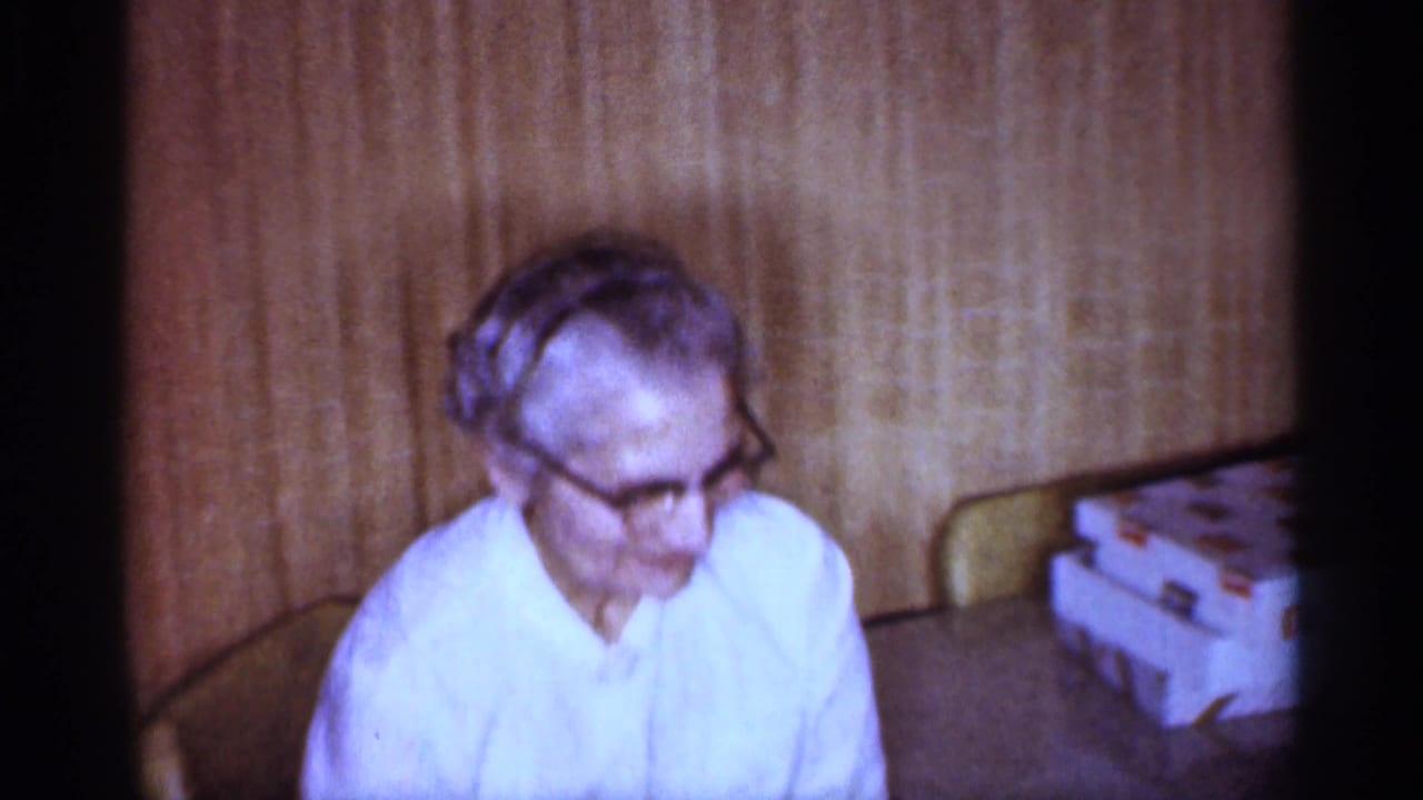 Older woman wearing glasses sits beside a table with stacked gift boxes.