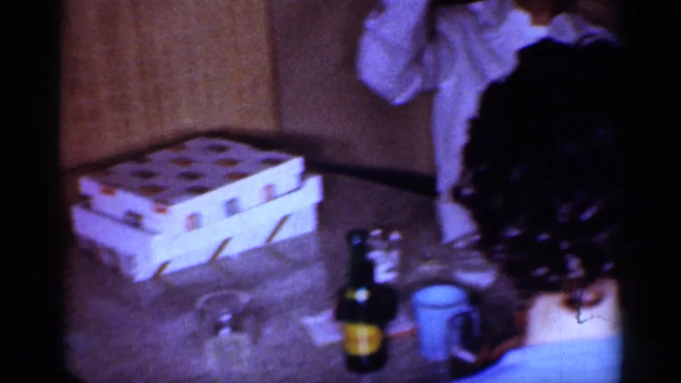 Indoor 1959 Michigan home-movie frame showing a party table with gift boxes, drinks, and adults gathered nearby.