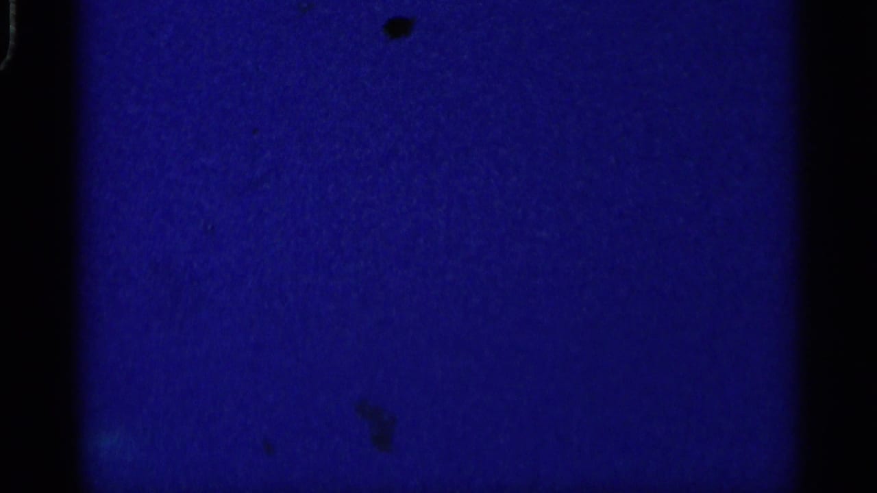 Blue-tinted blank or underexposed film frame with dark vertical borders and small specks.