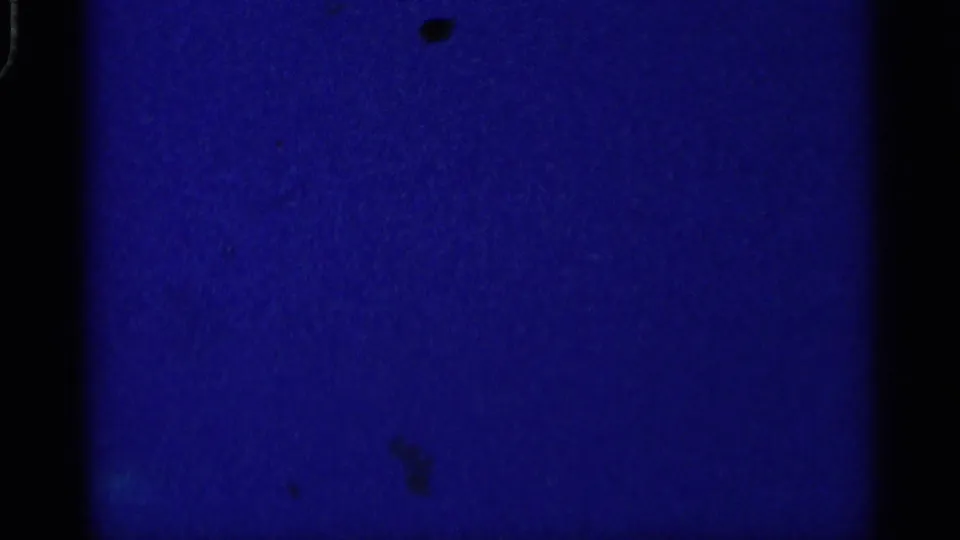 A mostly blue, underexposed 8mm frame with dark gate edges and dust marks, consistent with the beginning of the 1959 Michigan home-movie clip.