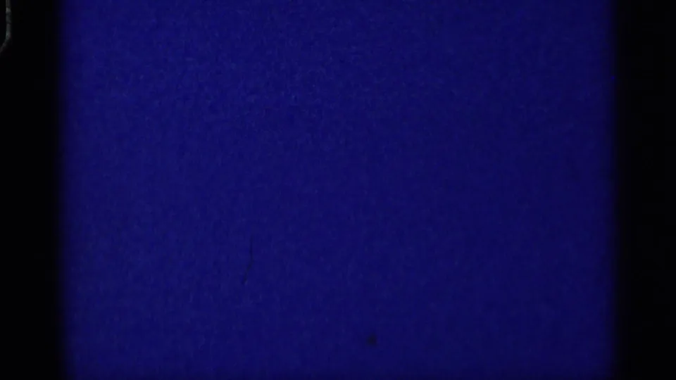 A mostly blue 8mm frame with visible grain and gate edges, preceding the visible indoor gathering in the supplied clip.