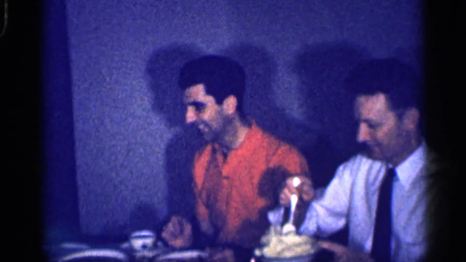 A 1959 Michigan dining-table moment shows one man serving mashed potatoes while another man watches and smiles.