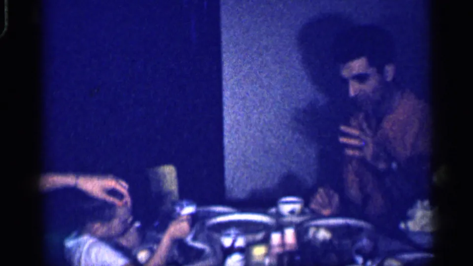 Near the end of the 1959 Michigan clip, a man sits at the dining table as another person reaches across the frame.
