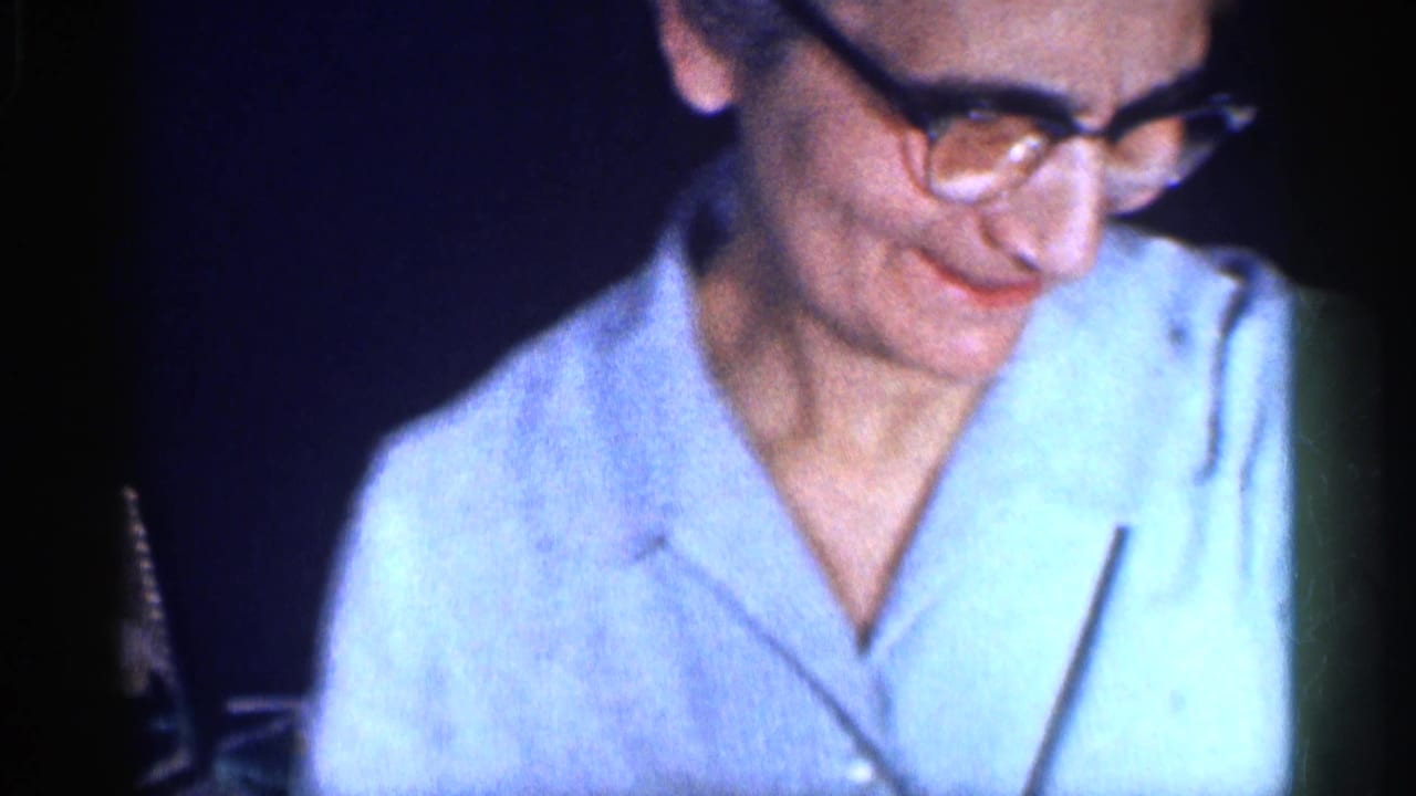 Close 8mm frame of a man in glasses and a light shirt looking down during a Michigan family meal scene.