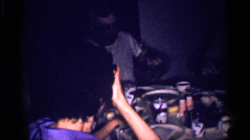1959 Michigan 8mm frame showing people gathered around a dimly lit dinner table in a private home.