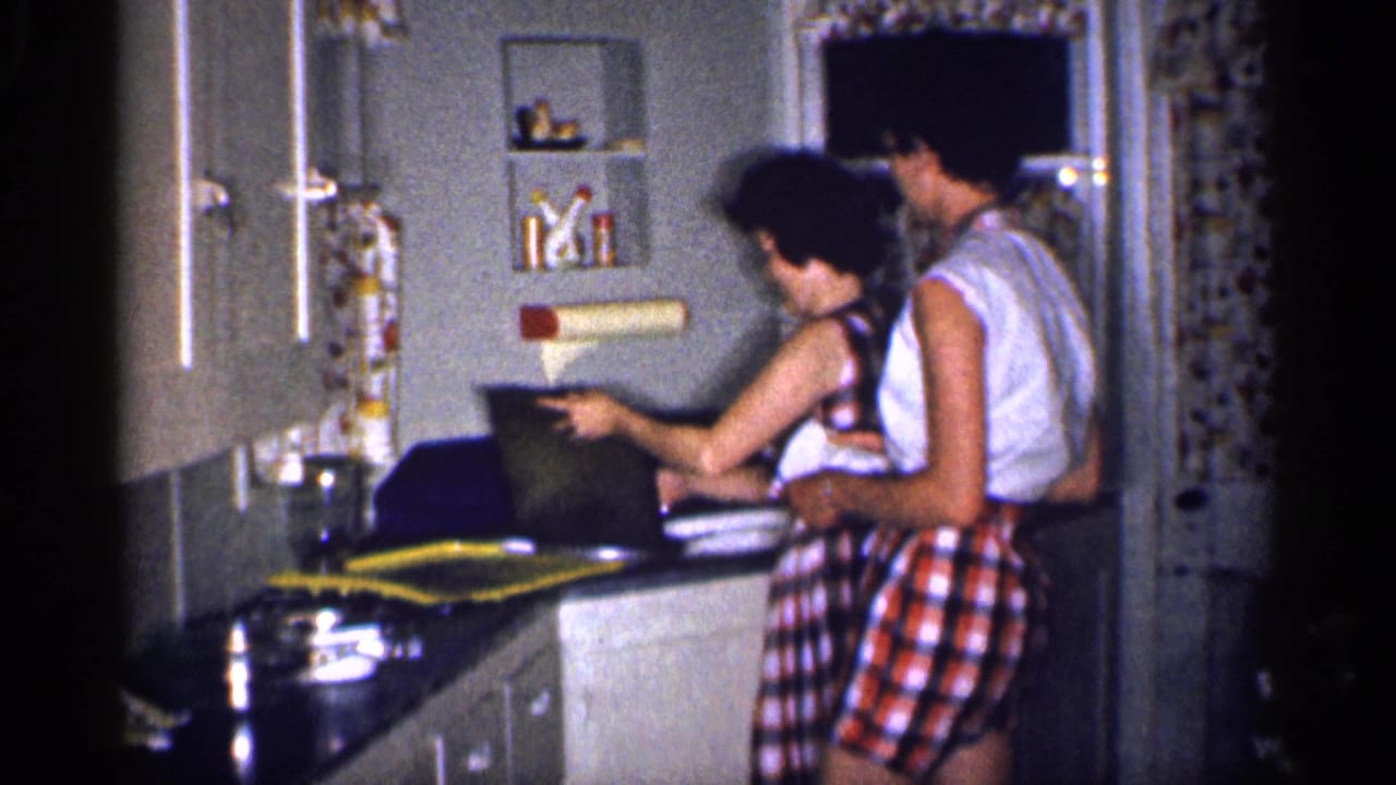Woman holds a dark pan or tray near the sink while the man stands beside her in the kitchen.