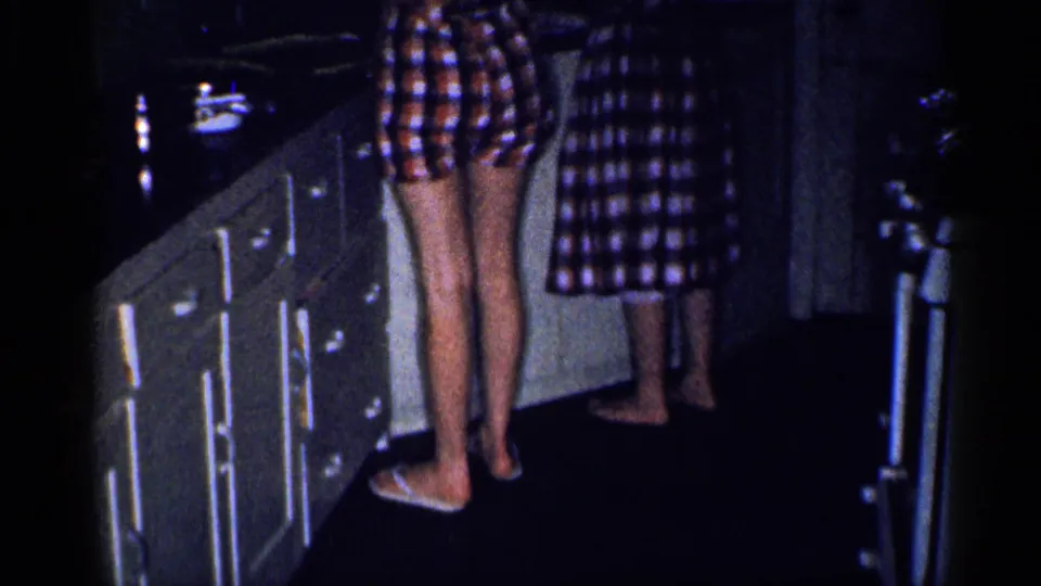1959 Michigan home-movie frame showing a woman and girl at a kitchen counter in matching plaid clothing.