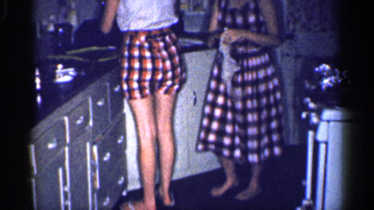 Home-movie frame of a girl and woman in matching plaid clothing working at a kitchen counter in Michigan, 1959.