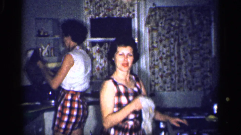 In the Michigan kitchen, one woman smiles toward the camera with a cloth while another stands at the counter.