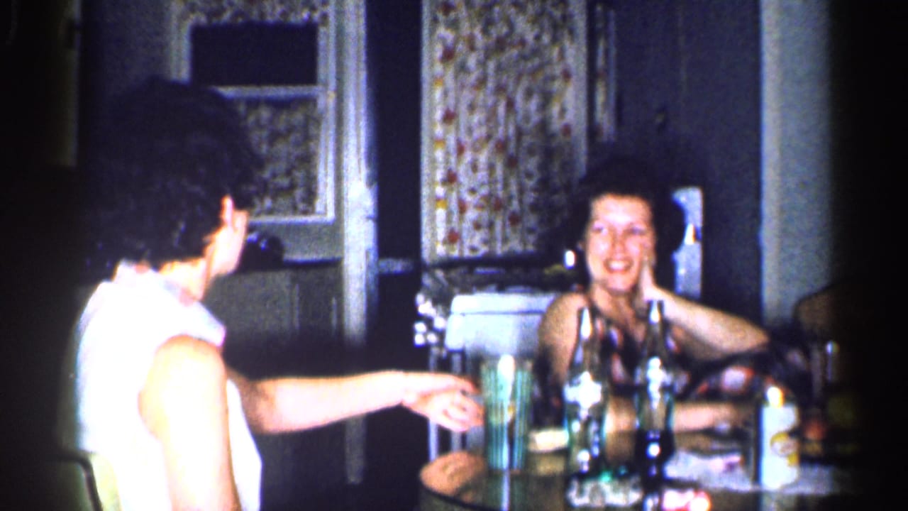 Two women sit at a kitchen table, one smiling toward the camera.