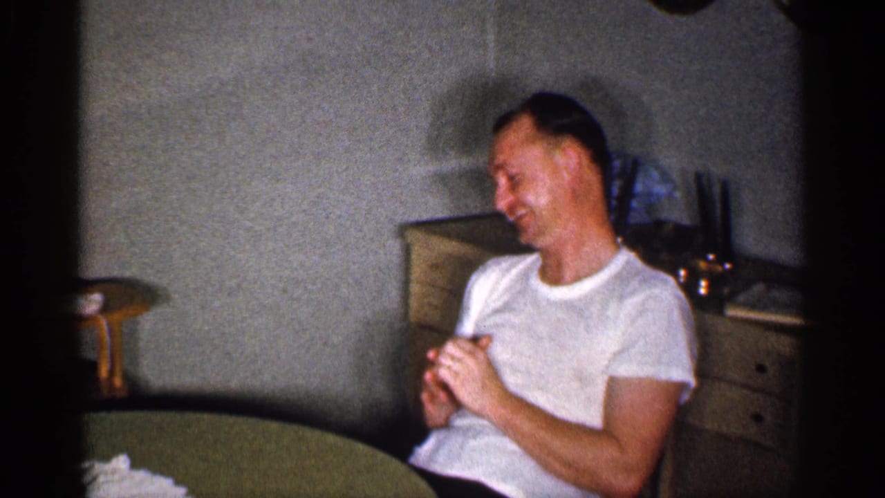 Seated man clasps his hands while smiling beside a round table.
