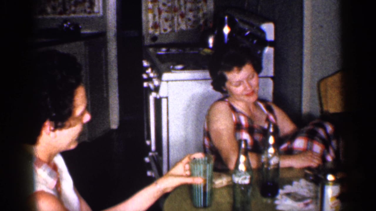 1959 Michigan kitchen scene with two women at a table, green glassware, bottles, and a retro white appliance in the background.