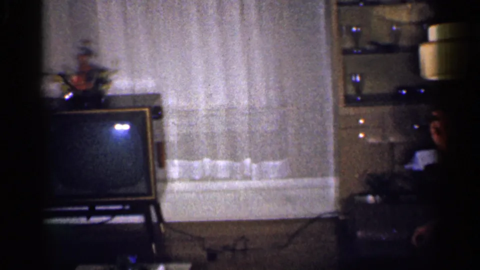 A 1959 Michigan living room frame shows a vintage television, curtains, cabinet, and the seated man partly visible at the edge.
