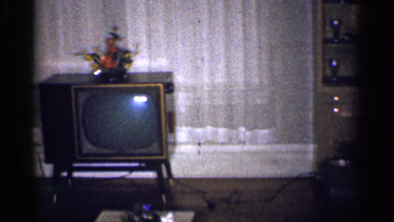 Living room with a box television on a stand, curtained windows, and furniture in soft 8mm focus.
