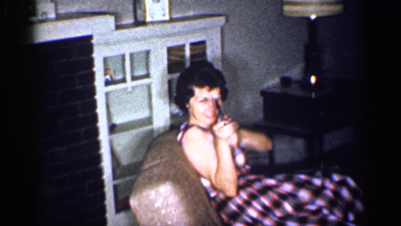 Woman seated in a plaid dress points a toy gun while looking toward the camera.