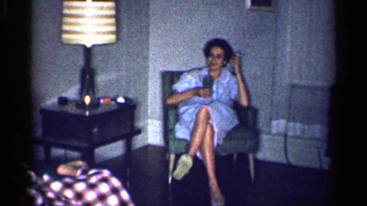 Woman in a light dress sits in an armchair while another woman reclines in the foreground.