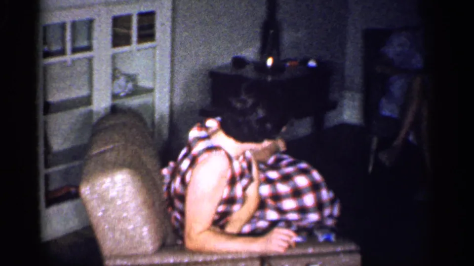 1959 Michigan indoor frame showing a woman in a checkered dress reclining while another woman sits near a cabinet.