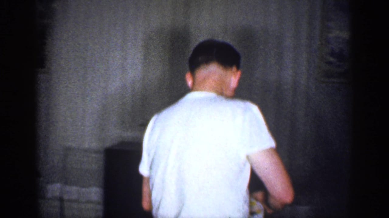 1959 Michigan home-movie frame showing an adult man from behind near a cabinet-style television in a private living room.